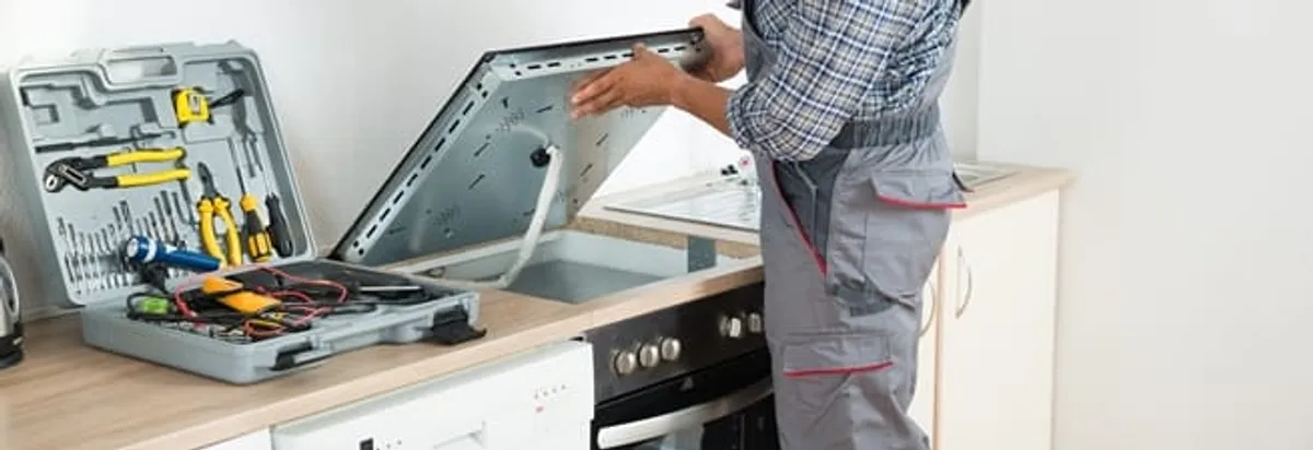 Cooktop repair technician lifting a built-in stovetop for service in Houston, TX